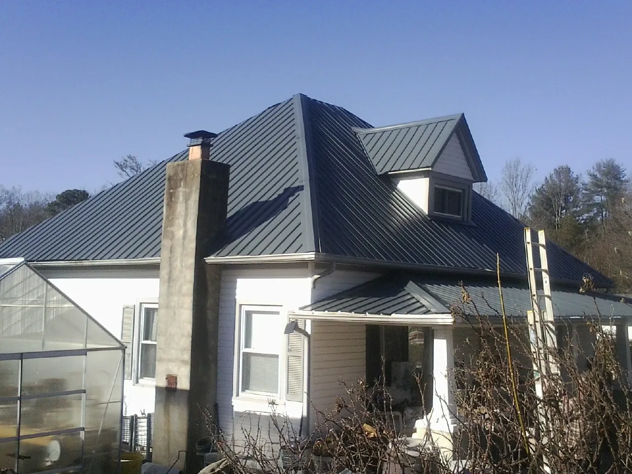 Dark blue standing seam metal roof on a white farmhouse with dormer — Slate & Tile Roof Repair by Roofing Brothers in Bellevue